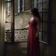 Woman in elegant red dress standing by an open window in a French hous... (thumbnail)