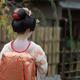 Maiko in white kimono with red collar showing skin makeup on the back... (thumbnail)