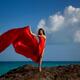 Woman in long red dress waving in the wind standing on a rocky sea sho... (thumbnail)