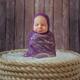 Cute sleepy newborn baby girl with a funny expression sitting bundled-... (thumbnail)