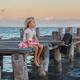 Little girl sitting on a wooden pier at the sea... (thumbnail)