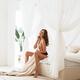 Beautiful sexy woman sitting on a bed topless holding a blanket in a b... (thumbnail)