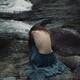 Woman sitting curled up by the river with her bare back exposed Dramat... (thumbnail)