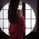 Asian woman in undone red kimono standing by a shoji window of a Japan... (thumbnail)