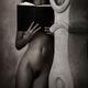 Young lady standing naked with a book leaning against an antique clock... (thumbnail)
