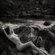 Beautiful nude woman lying on rocks by a river in nature scenery Black... (thumbnail)