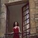 Young woman in red dress standing in an open balcony window of an old... (thumbnail)
