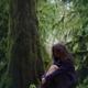 Woman with thoughtful contemplative expression sitting on mossy tree t... (thumbnail)