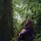 Woman with a dreamy expression sitting on a mossy tree trunk in ancien... (thumbnail)