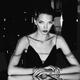 Seductive woman in sexy black dress sitting at restaurant table, edgy... (thumbnail)