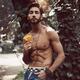 Sexy handsome man with bare torso leaning against a tree holding a yel... (thumbnail)