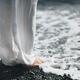 Woman in white standing on a pebble shore, cool sea water washing over... (thumbnail)