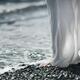 Woman in white summer pants standing barefoot on a pebbled ocean beach... (thumbnail)