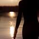 Dark silhouette of a woman walking into the sea at sunset her hand tou... (thumbnail)