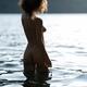 Beautiful nude woman with curly hair standing in reflective water of a... (thumbnail)