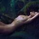 Beautiful nude woman lying relaxed on a mossy tree in dark forest with... (thumbnail)