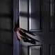 Spooky male hand reaching for a door handle from behind a door in a da... (thumbnail)
