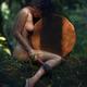 Beautiful nude woman sitting in a tranquil nature scenery leaning agai... (thumbnail)