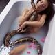 Beautiful sexy woman taking a bath holding a large boa snake against h... (thumbnail)