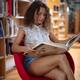 Pretty, young lady, college student reading a book in a library sittin... (thumbnail)