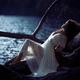 Woman in sheer white lace dress reclining against a tree by the lake i... (thumbnail)