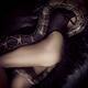 Black boa constrictor snake coiled around sensual woman body enveloping her thighs and buttocks on black bed