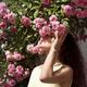 Beautiful woman standing under a bush of pink roses smelling the flowe... (thumbnail)