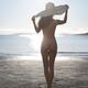 Sexy sun-tanned naked young woman in a big sun hat standing at a sandy... (thumbnail)