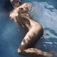 Beautiful nude woman lying in blue water with water droplets on her we... (thumbnail)