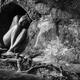 Fine art nude photograph of a naked woman sitting curled up in rock ca... (thumbnail)