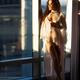 Beautiful woman in white lace night gown standing half naked with a gl... (thumbnail)