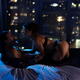 Sensual couple making love on a bed by a large window with night city... (thumbnail)