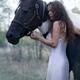 Beautiful girl with long curly dark hair hugging a black and white hor... (thumbnail)