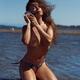 Beautiful topless young woman in bikini kneeling in shallow sea water... (thumbnail)