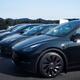 Black Tesla Model Y followed by Tesla 3 electric cars parked outdoors... (thumbnail)