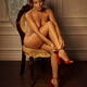 Beautiful young woman sitting naked in a chair putting on red high hee... (thumbnail)