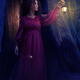 Woman in red dress walking with a lit lantern in her hand in a dark fo... (thumbnail)