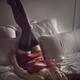 Woman lying on a bed in sexy red silk nightgown with her long legs in... (thumbnail)