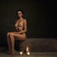 Beautiful nude woman sitting on the edge of a stone bath with candles... (thumbnail)