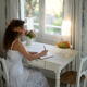 Young woman in white summer dress writing in a diary sitting at a tabl... (thumbnail)