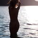 Dark silhouette of a nude woman entering lake water at sunset rear vie... (thumbnail)
