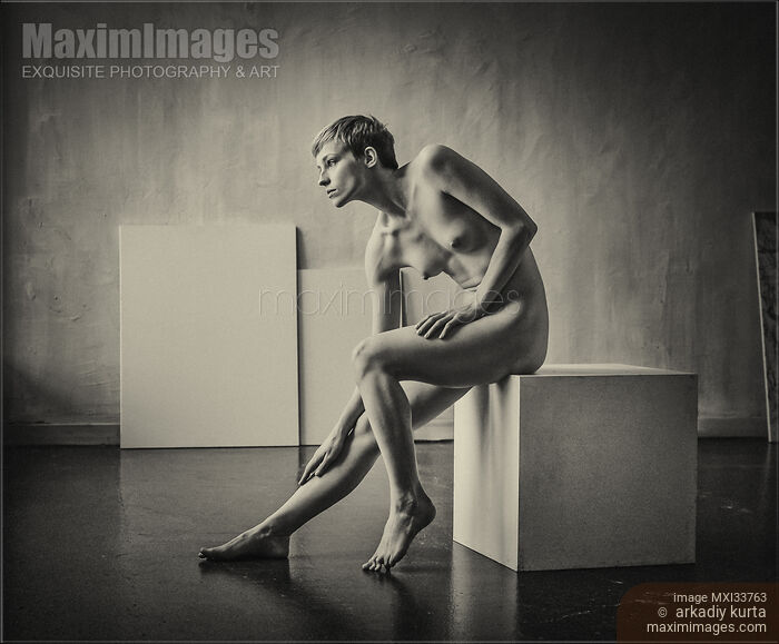 Stock photo of Art nude portrait of woman sitting naked on a posing box in artist studio. Black and white sepia. Buy commercial use license at MaximImages