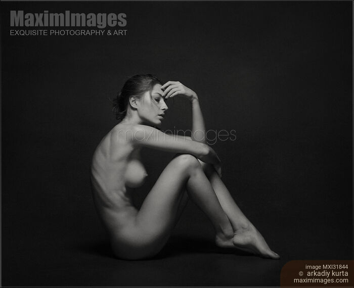 Stock photo of Art nude side view of a woman sitting naked in studio with black background Buy commercial use license at MaximImages