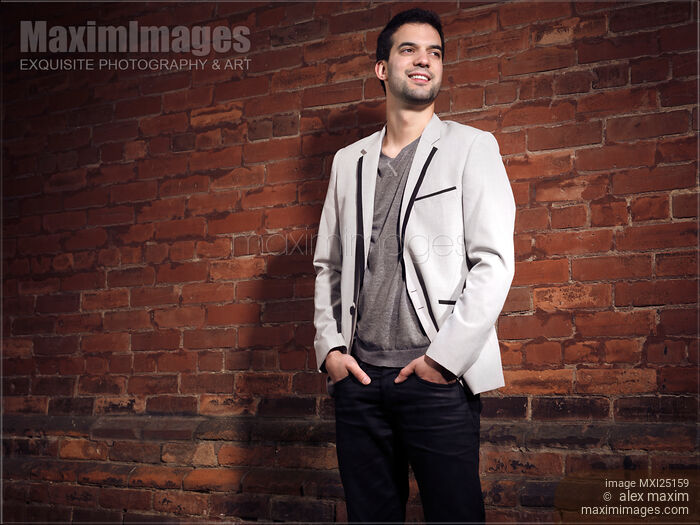 Stock photo of Artistic portrait of a smiling young man at brick wall Buy commercial use license at MaximImages