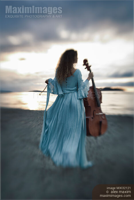 Atmospheric portrait of a woman in a vintage dress standing with a cello on an ocean shore in the wind in dramatic sunset Stock photo of Atmospheric portrait of a woman in a vintage dress standing with a cello on an ocean shore in the wind in dramatic sunset Buy commercial use license at MaximImages