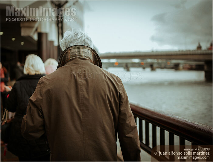 Stock photo of Back of a grey-haired man in winter jacket walking along the river in London moody city scenery Buy commercial use license at MaximImages