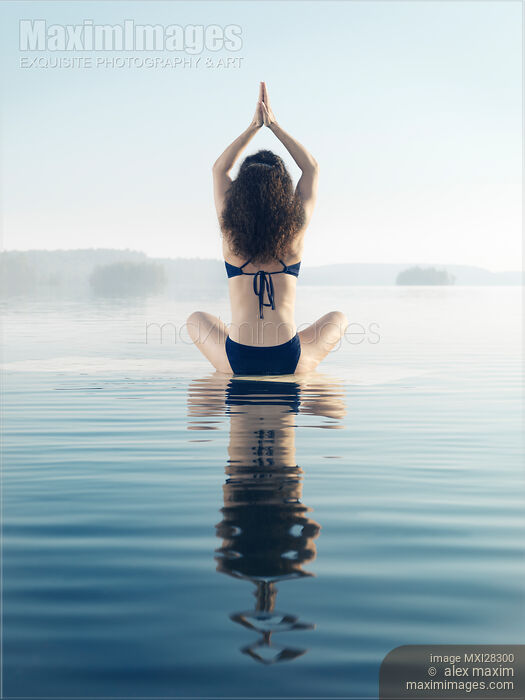Stock photo of Back of a woman practicing yoga meditation on the water in sunrise mist Buy commercial use license at MaximImages