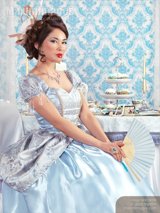 Stock photo of Beautiful asian lady sitting with a fan at a table Buy commercial use license at MaximImages