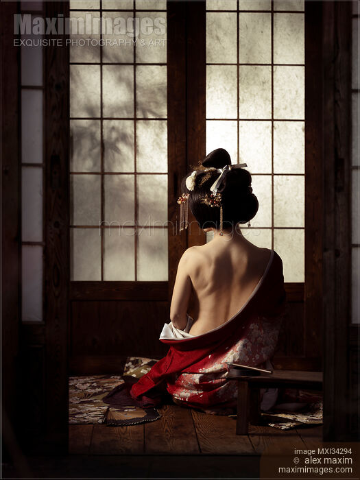 Stock photo of Beautiful geisha sitting in undone red kimono revealing her bare back Buy commercial use license at MaximImages