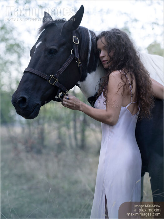 Beautiful girl with long curly dark hair hugging a black and white horse. Expressive candid portrait. Stock photo of Beautiful girl with long curly dark hair hugging a black and white horse. Expressive candid portrait. Buy commercial use license at MaximImages